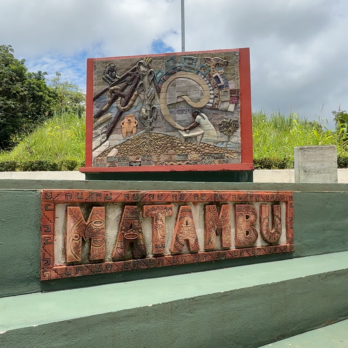 Decorative sign for Matambú indigenous territory in Costa Rica with text and artwork on a green steps in a park-like setting